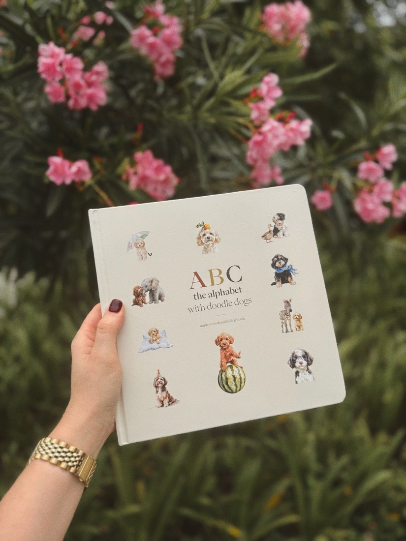 The ABC Doodle Dogs book held in front of pink flowers